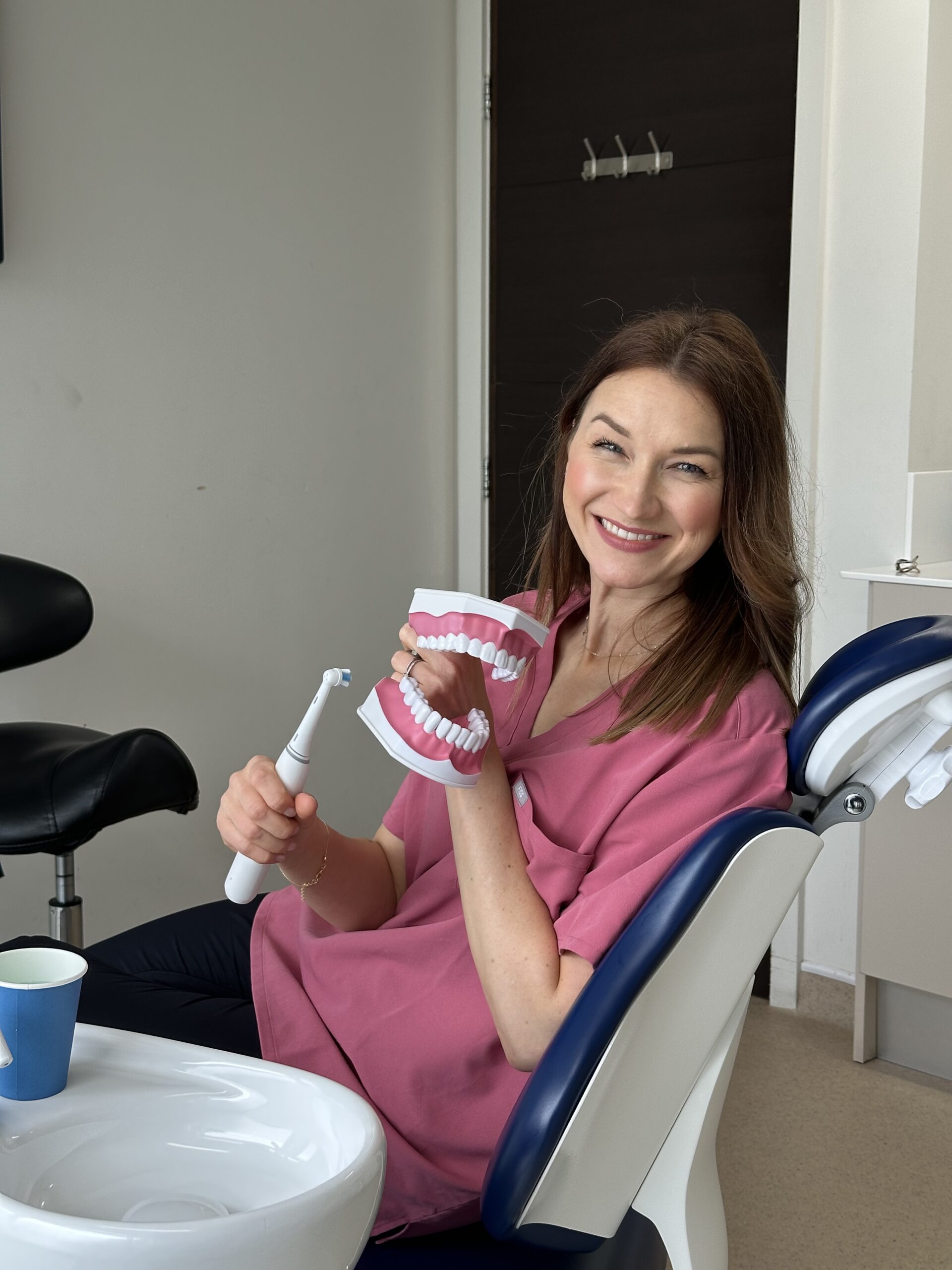Kasia Velaj, edukatorka zdrowia jamy ustnej, uśmiecha się i trzyma model szczęki oraz szczoteczkę
